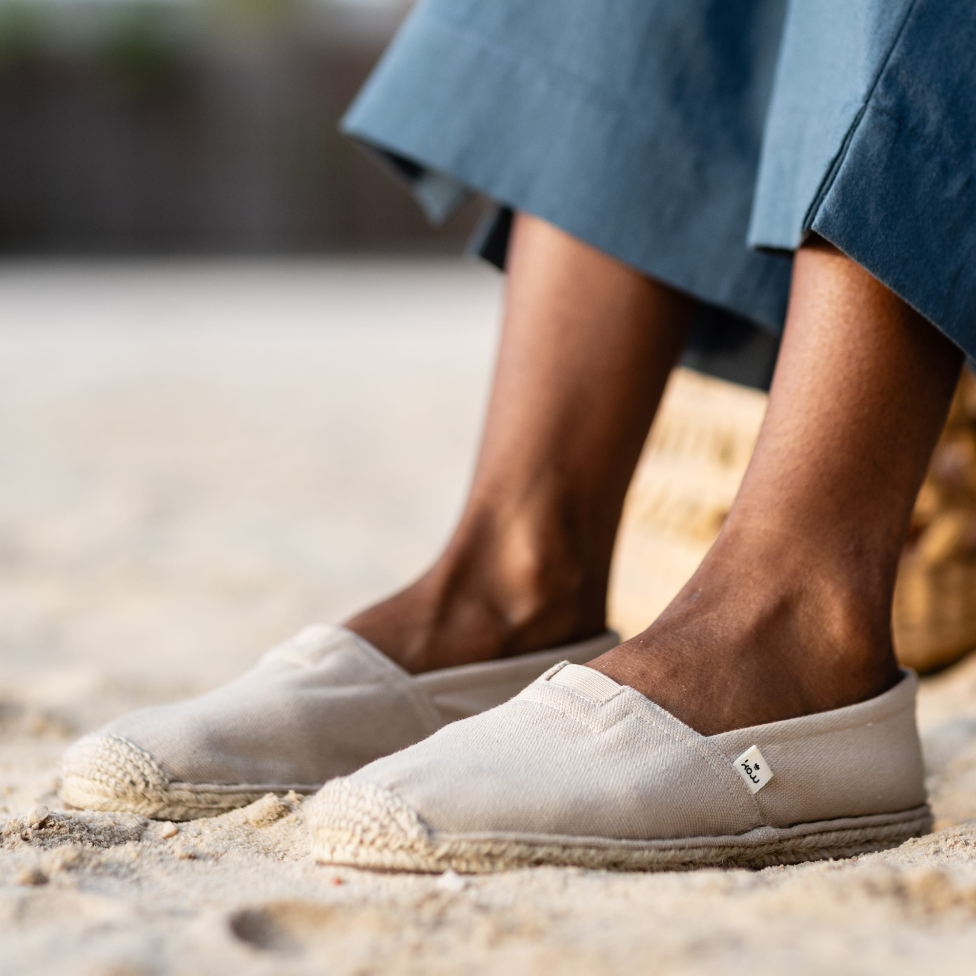 Beige espadrille shoes worn on feet standing on sand with blurred background