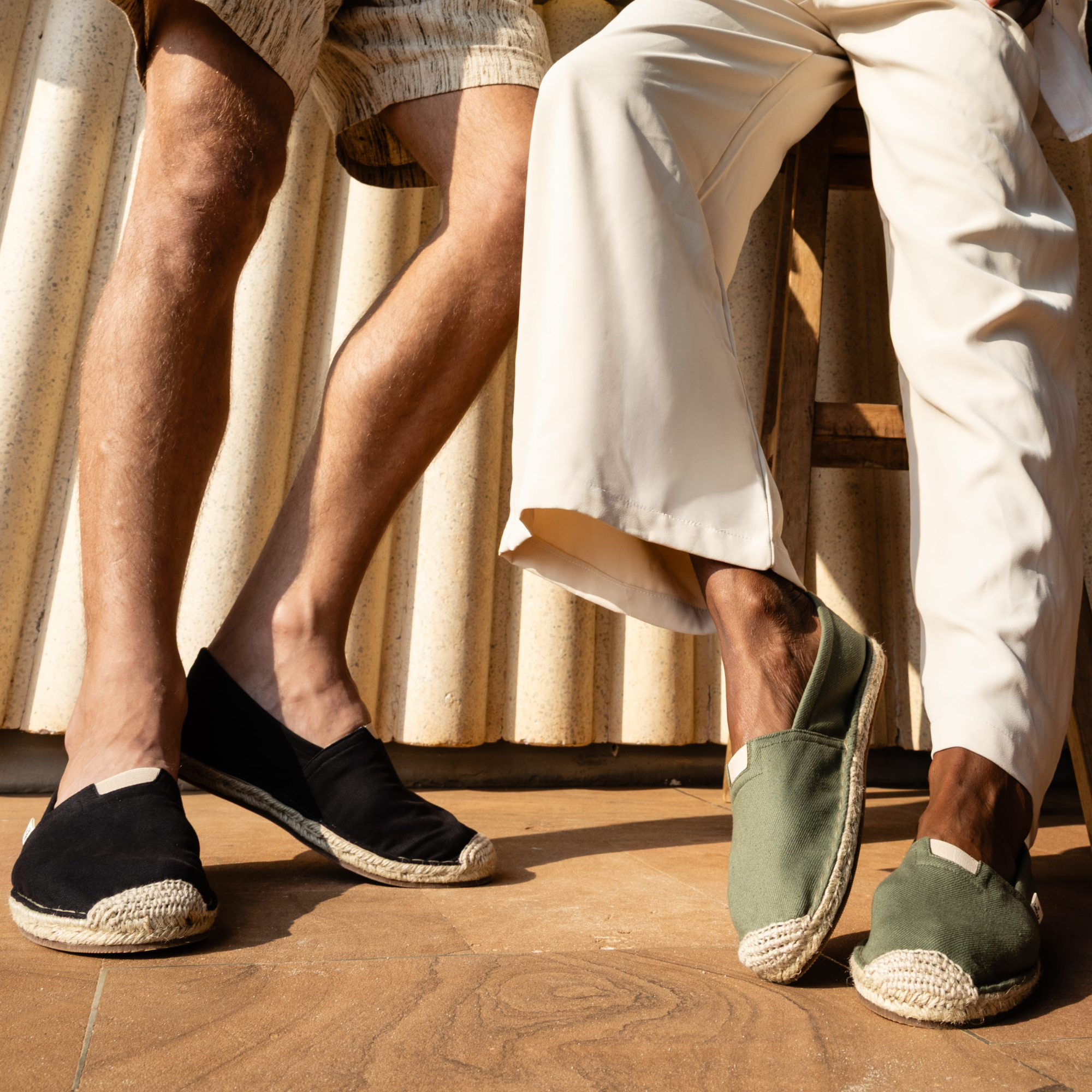 Two pairs of feet wearing espadrilles on a wooden floor.