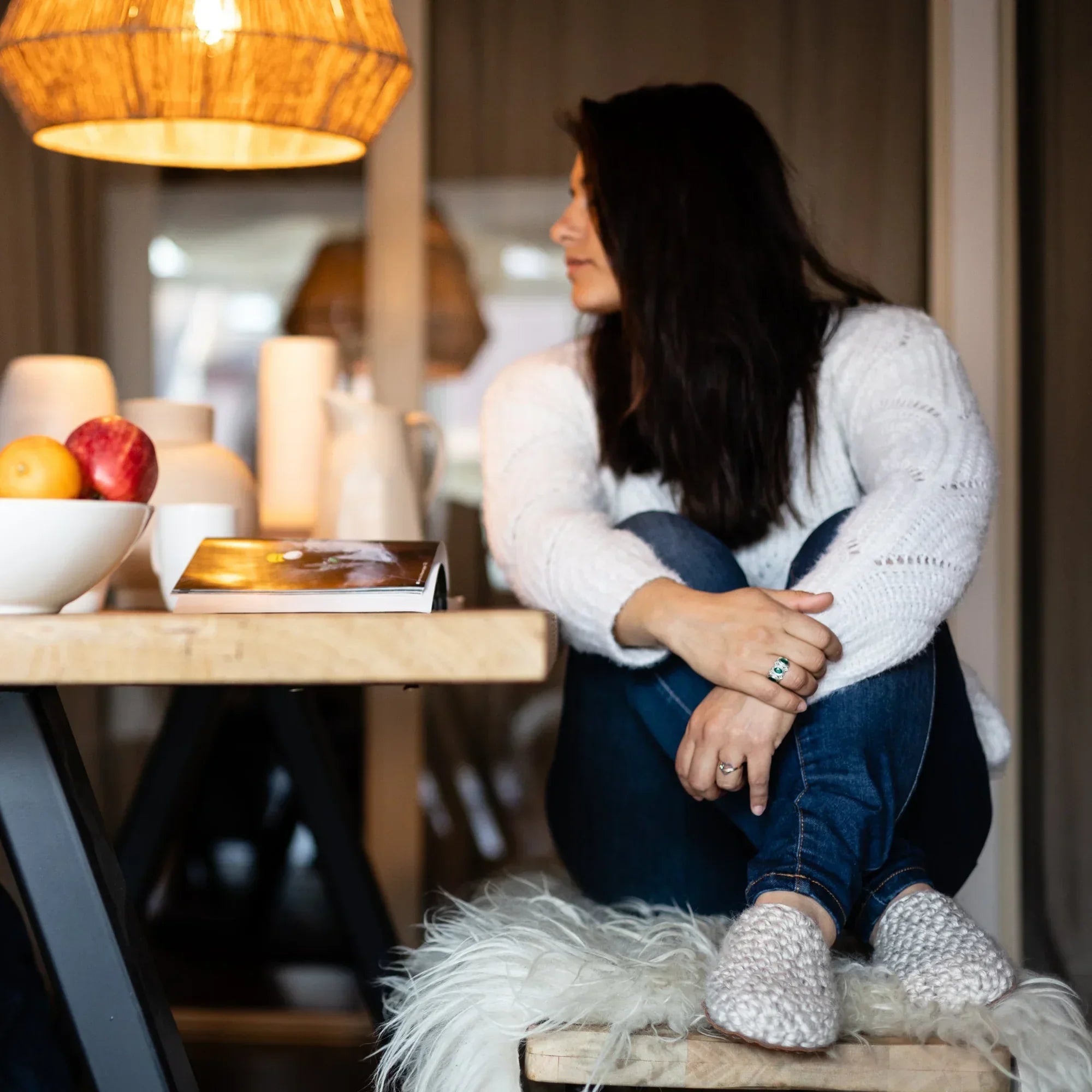 Woman sitting on a stool in a cozy room wearing beige wool slippers
