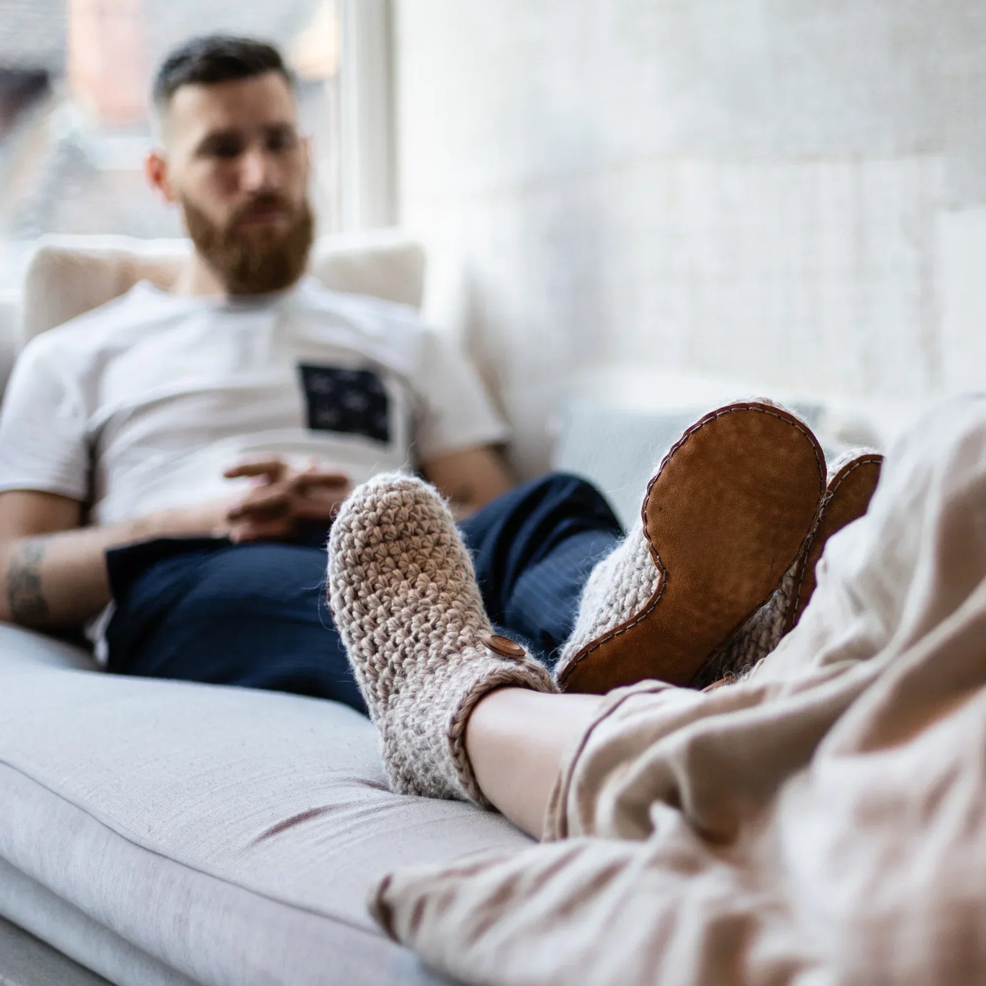 Person wearing cozy slippers sitting on a couch with another person in the background.