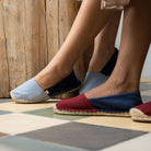 Two pairs of feet wearing colorful espadrilles on a checkered floor.