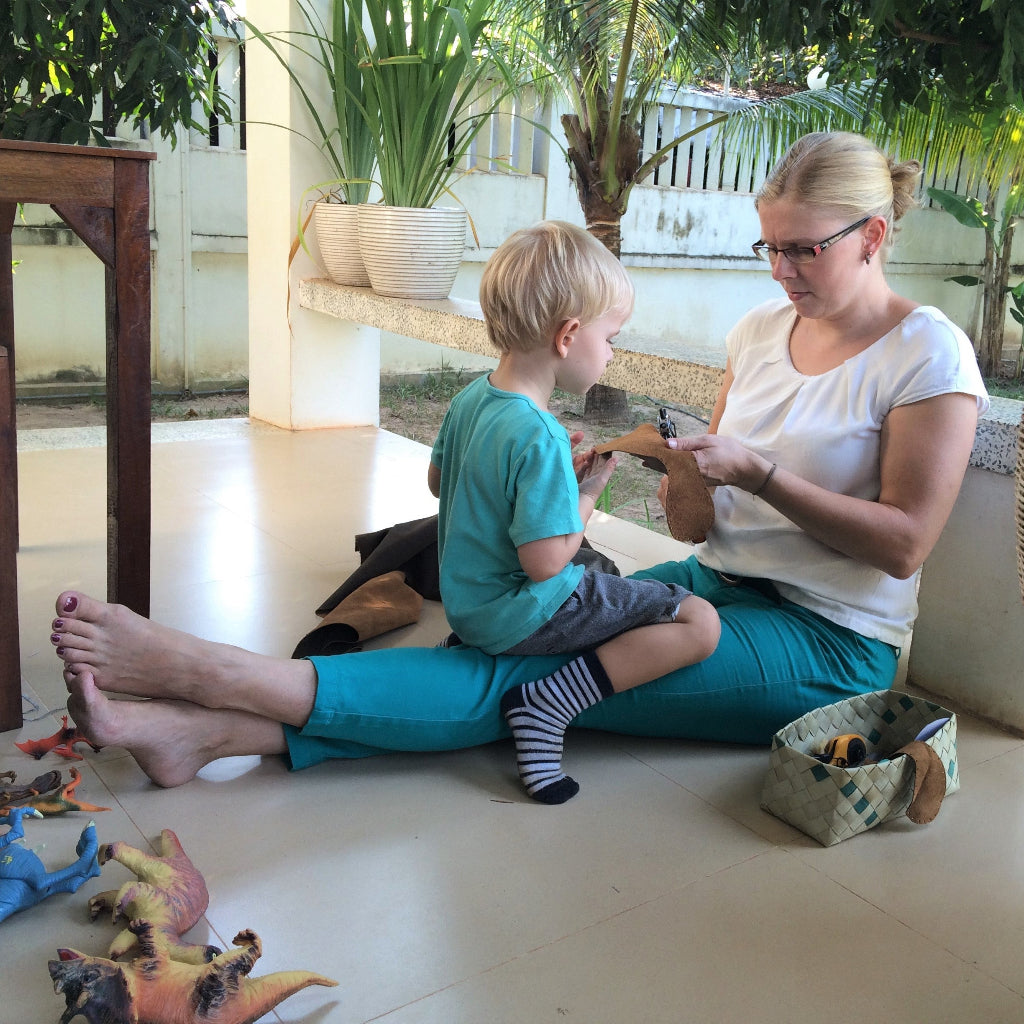 Godie (founder) inspecting a leather sole with her son on her lap in the early days of KOW