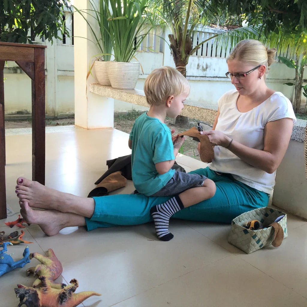 Godie (founder) inspecting a leather sole with her son on her lap in the early days of KOW