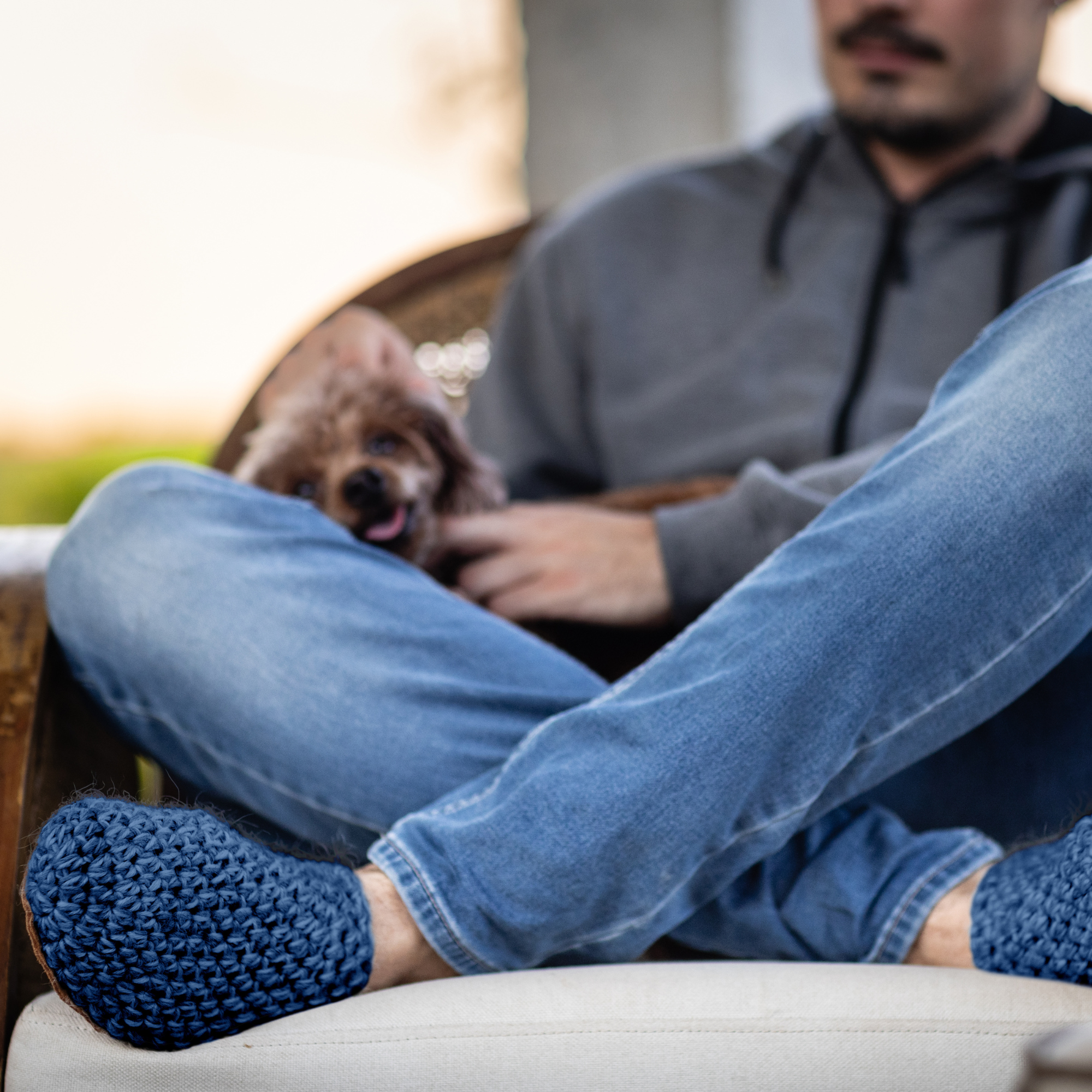 Person sitting on a couch with a dog in their lap, wearing blue wool slippers.