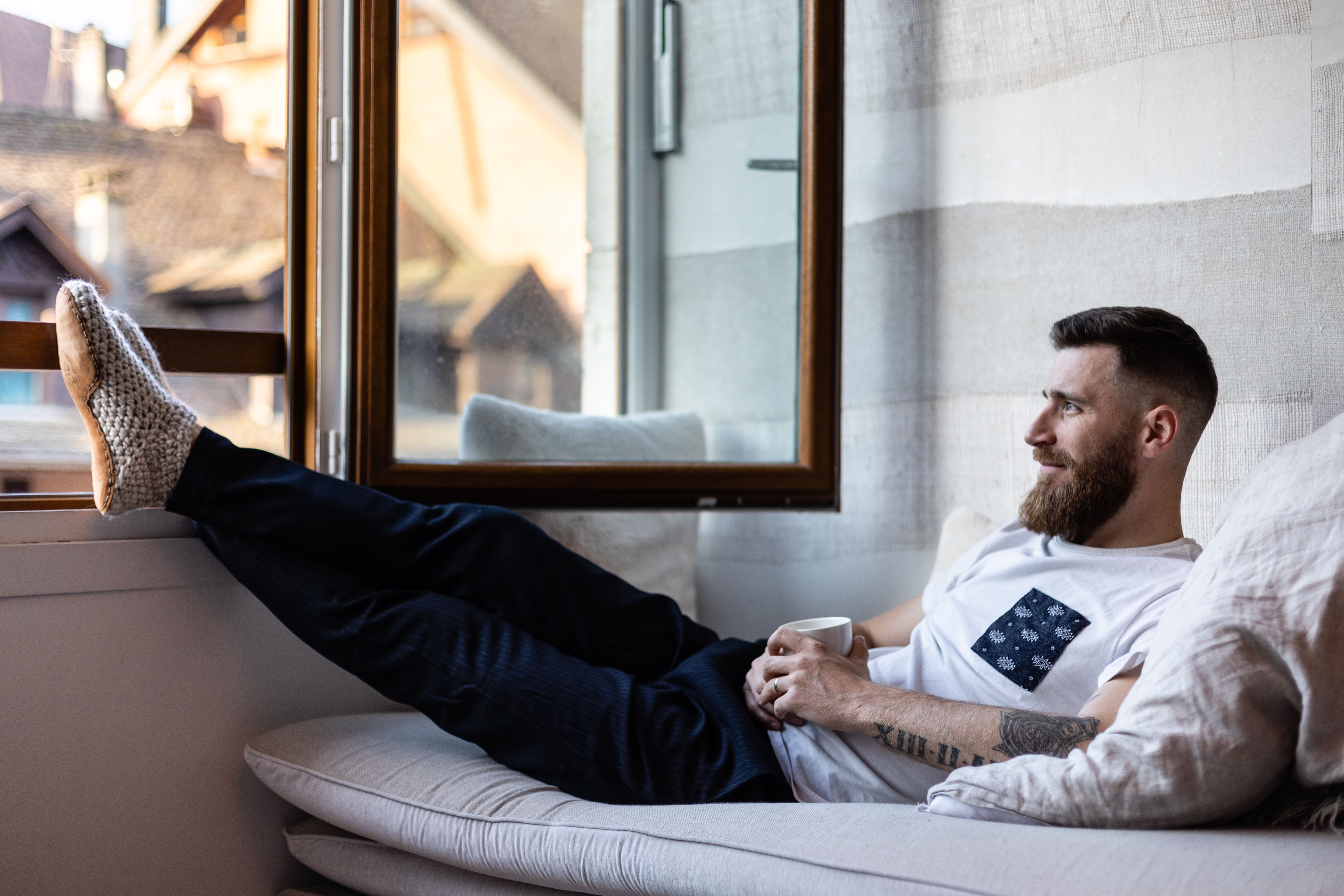Man wears Kingdom of Wow Chai Bootie Slippers with legs on window sill