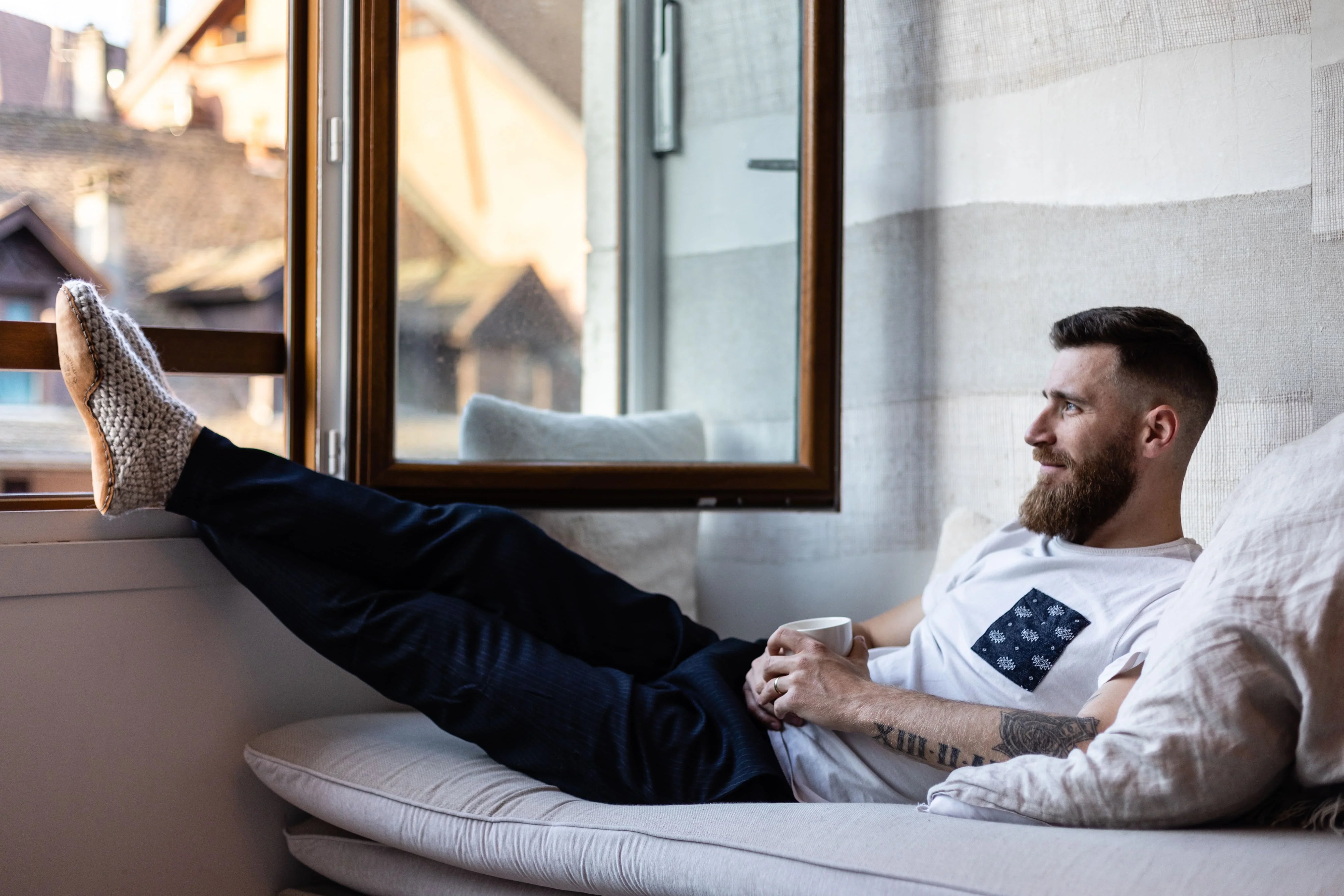 Man wears Kingdom of Wow Chai Bootie Slippers with legs on window sill