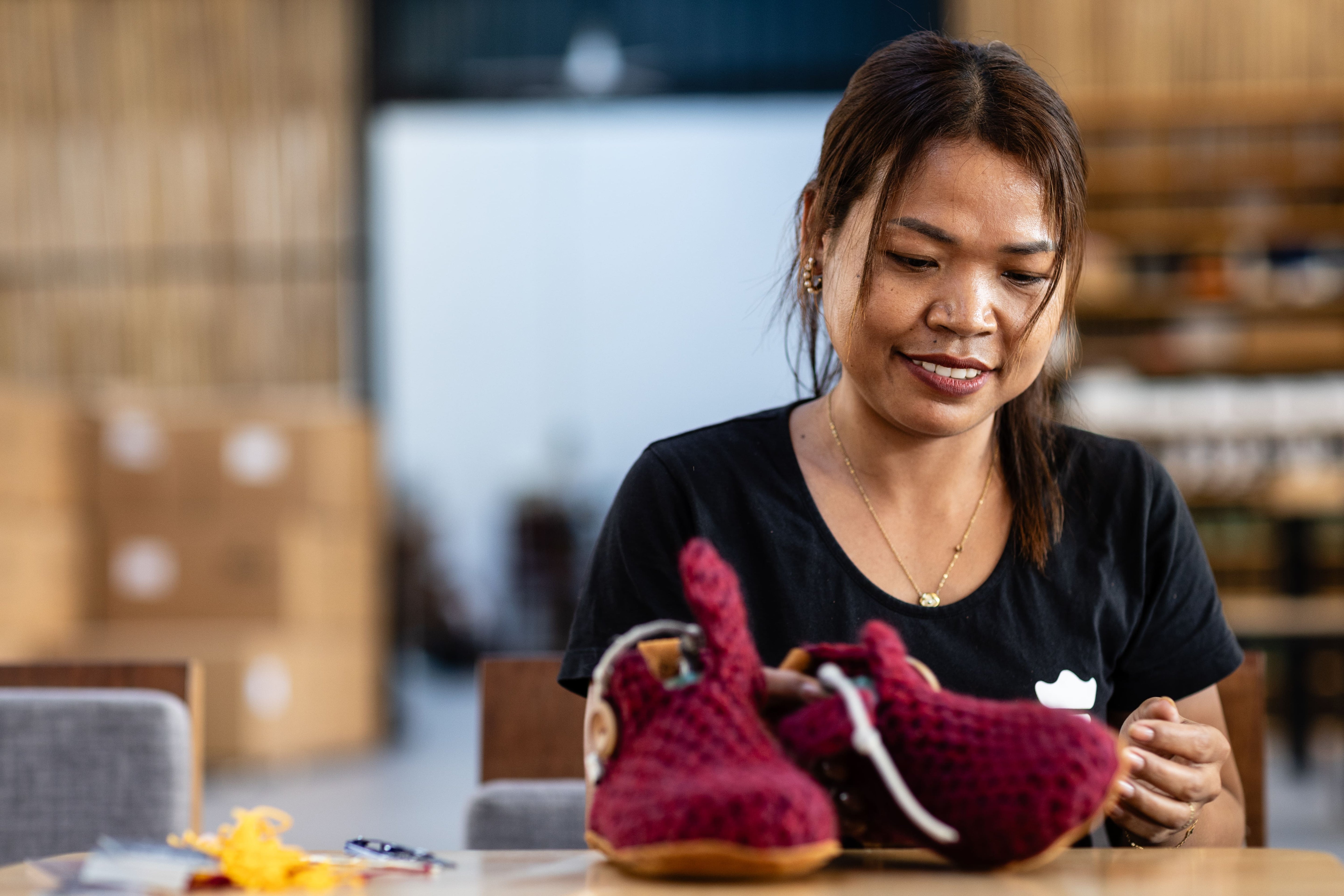 Woman sitting checking the quality of red wool slippers in a warehouse setting