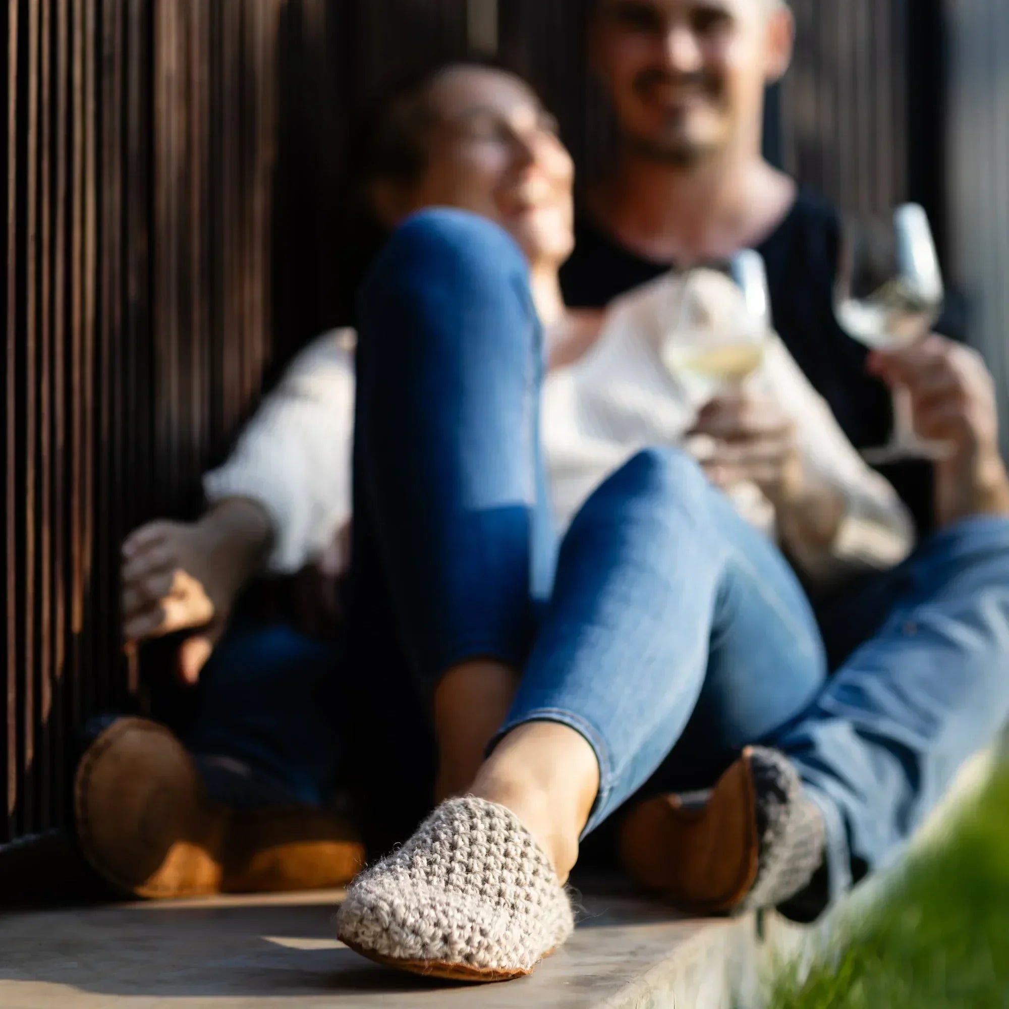Two people sitting together wearing light wool slippers. Enjoying a glass of wine in the late evening sun.
