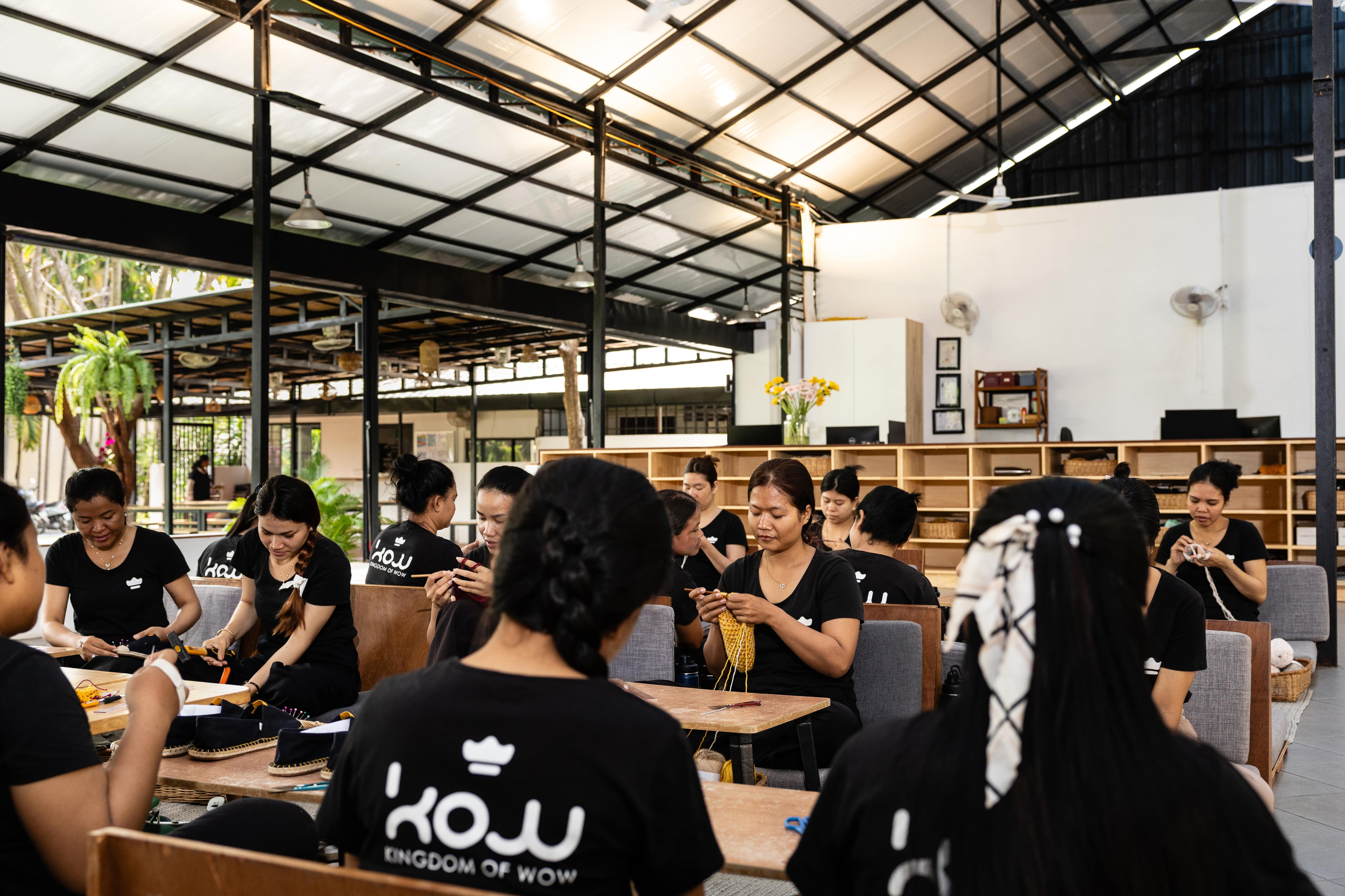 Group of people sitting in a modern manufacturing workshop, wearing 'KOW' branded t-shirts.