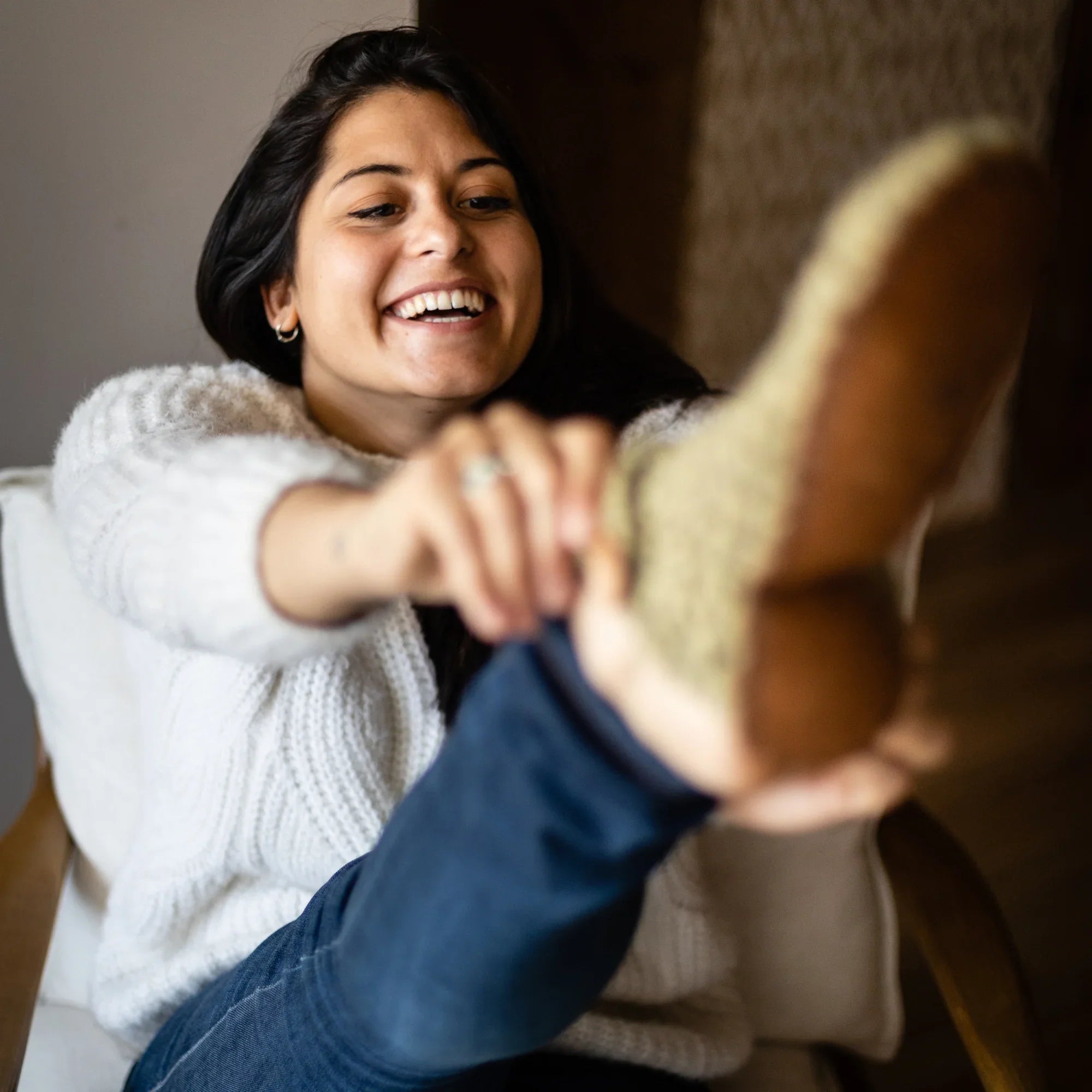 Woman smiling as she receives a gift of wool slippers from another person.