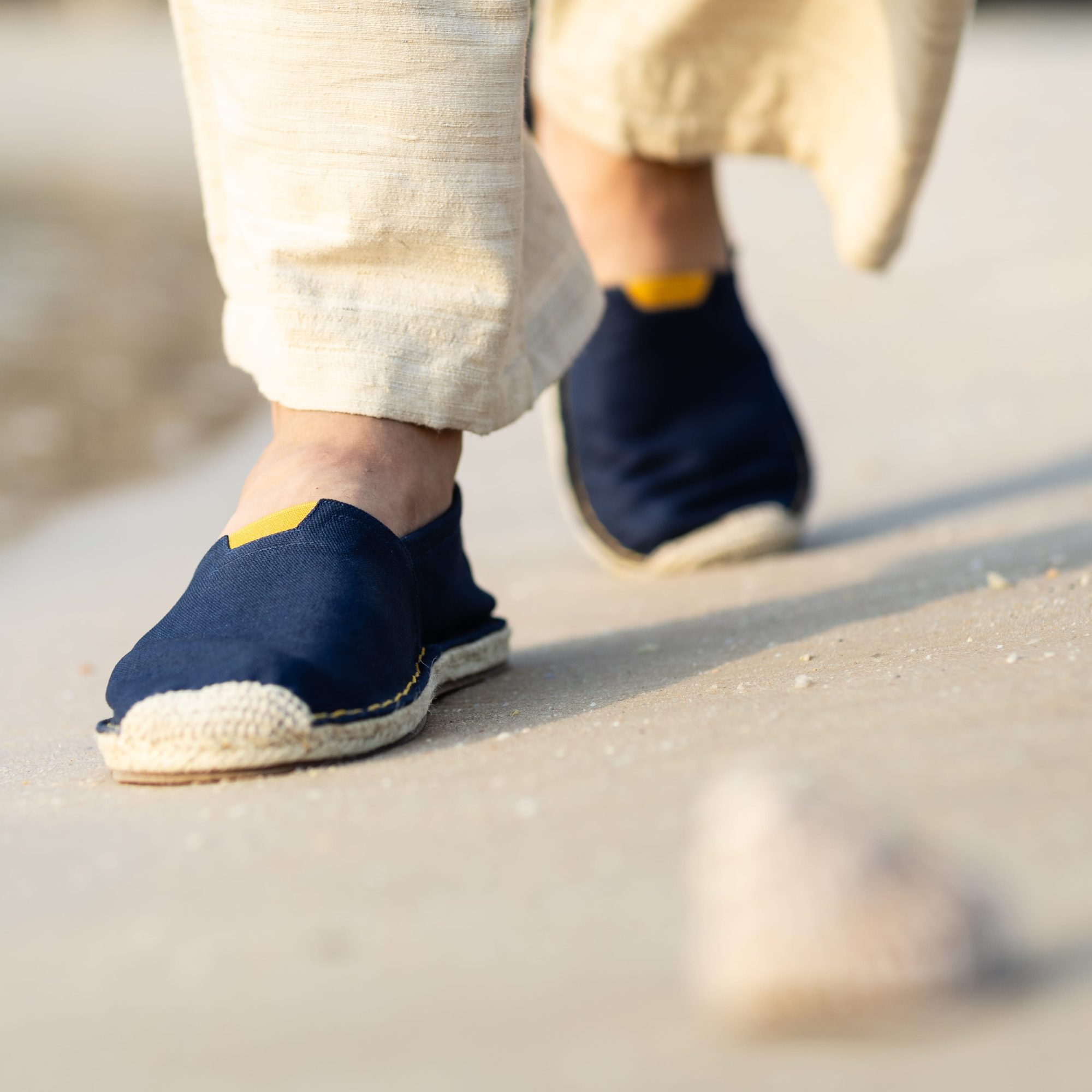 Navy blue espadrilles with yellow accents worn on a beach