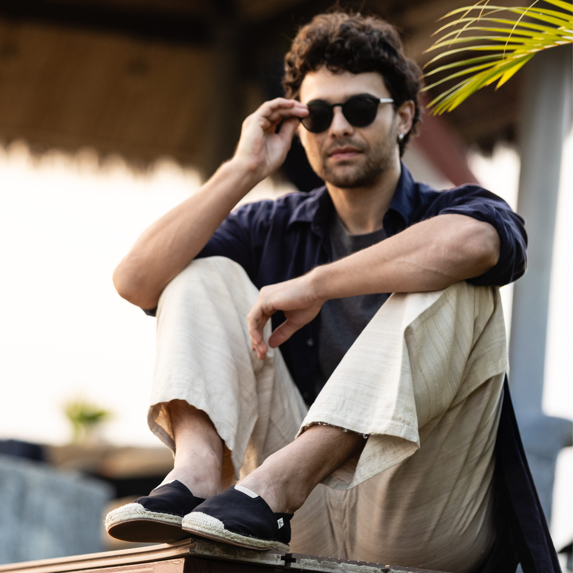 Man sitting outdoors wearing sunglasses, casual clothing and espadrille shoes