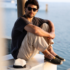 Man sitting by the water wearing sunglasses, casual clothing and summer espadrilles
