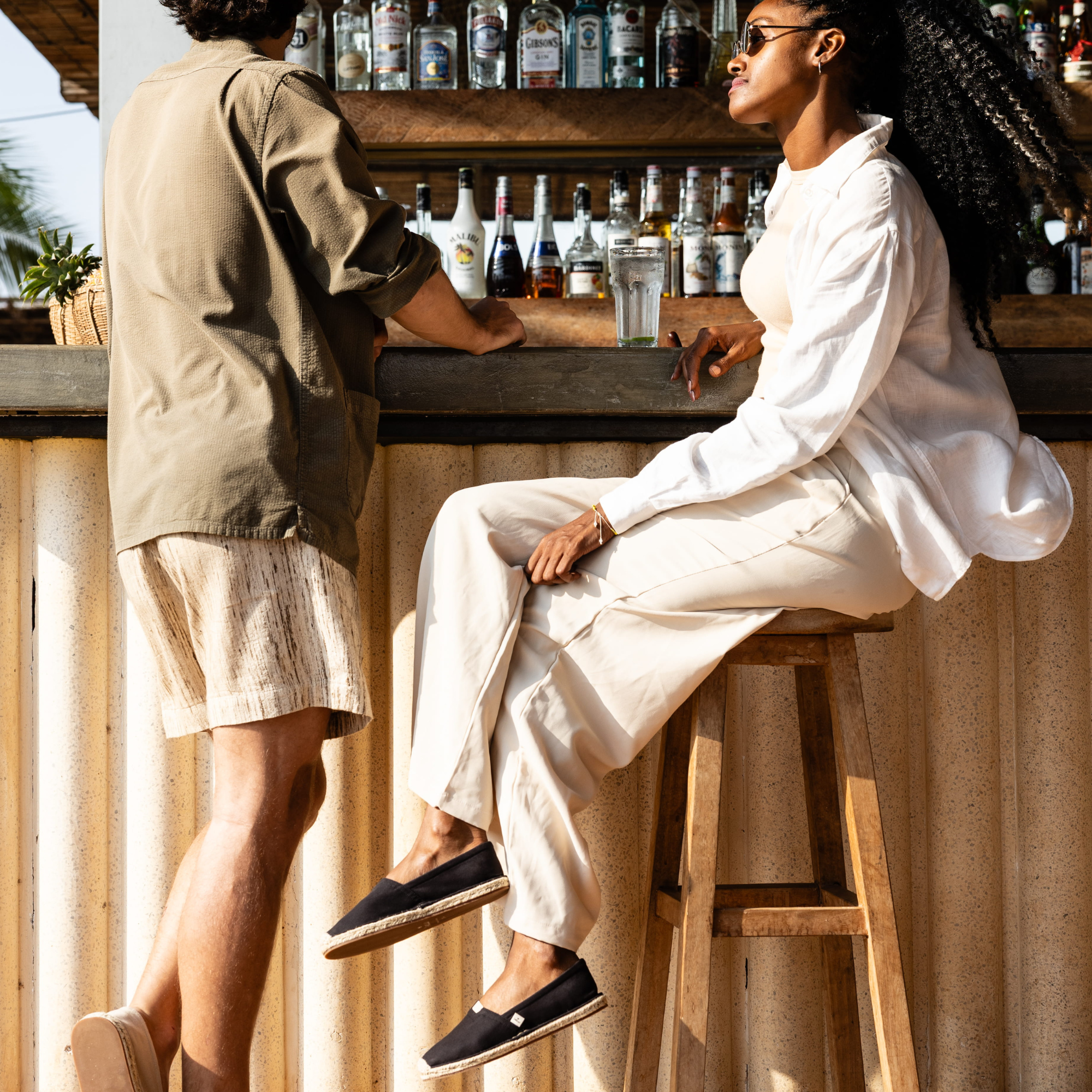 Two people at a bar with drinks and bottles in the background