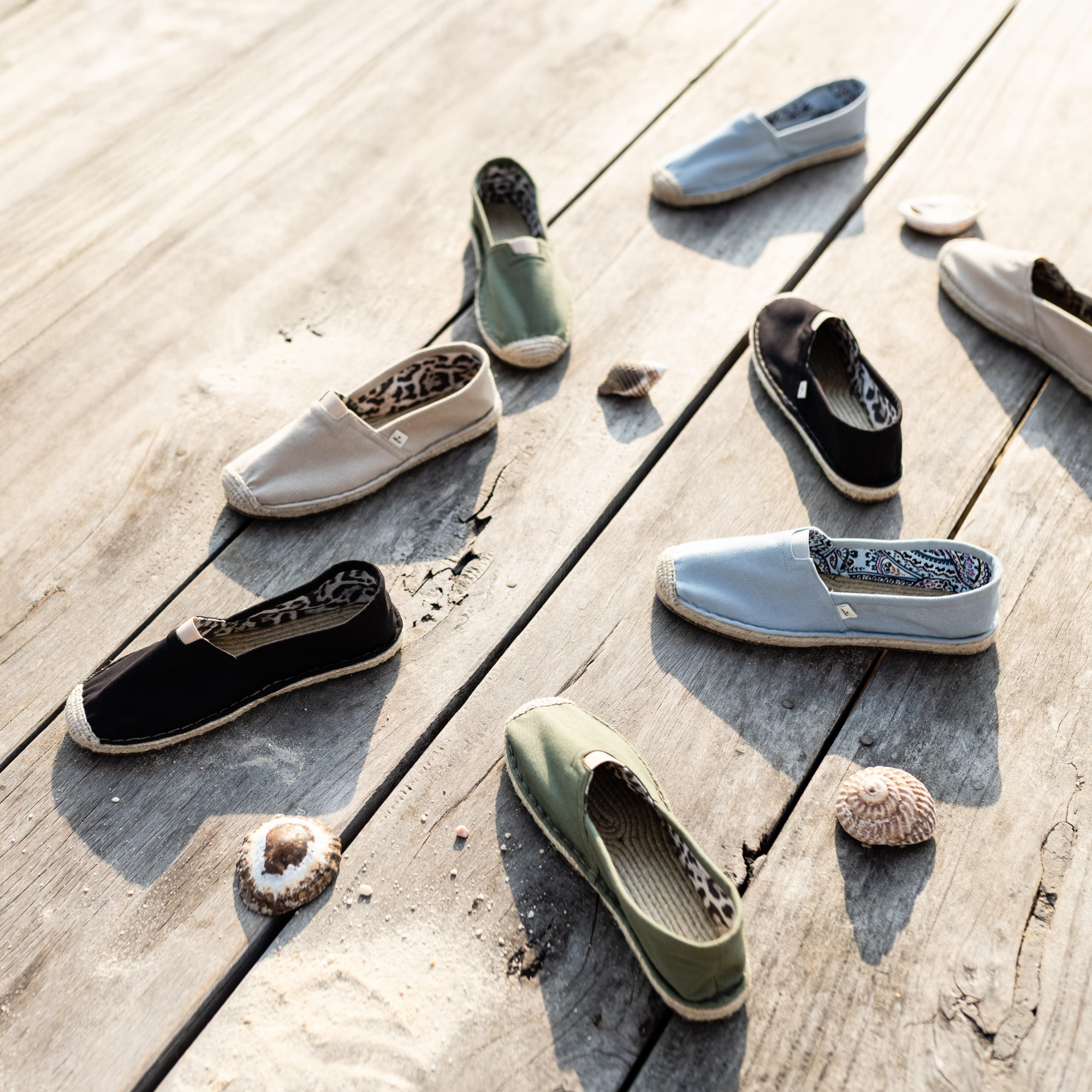 Various cotton espadrlles on a wooden surface with seashells.