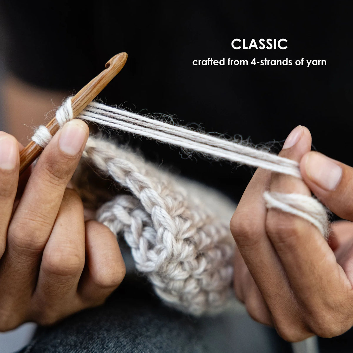 Close-up of hands crocheting with a wooden crochet hook and off-white yarn, with text reading 'CLASSIC crafted from 4-strands of yarn' on a dark background.