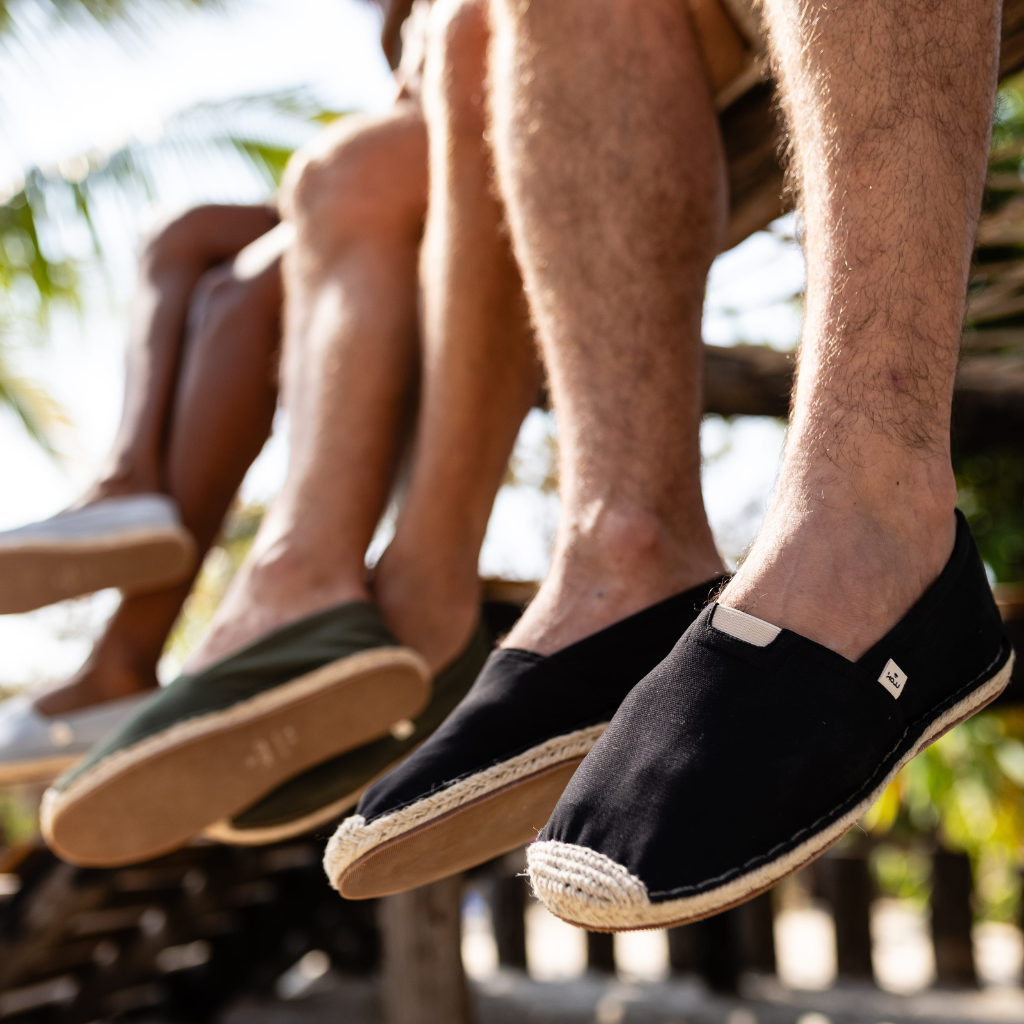 Two pairs of feet wearing black and green espadrilles with a blurred outdoor background.