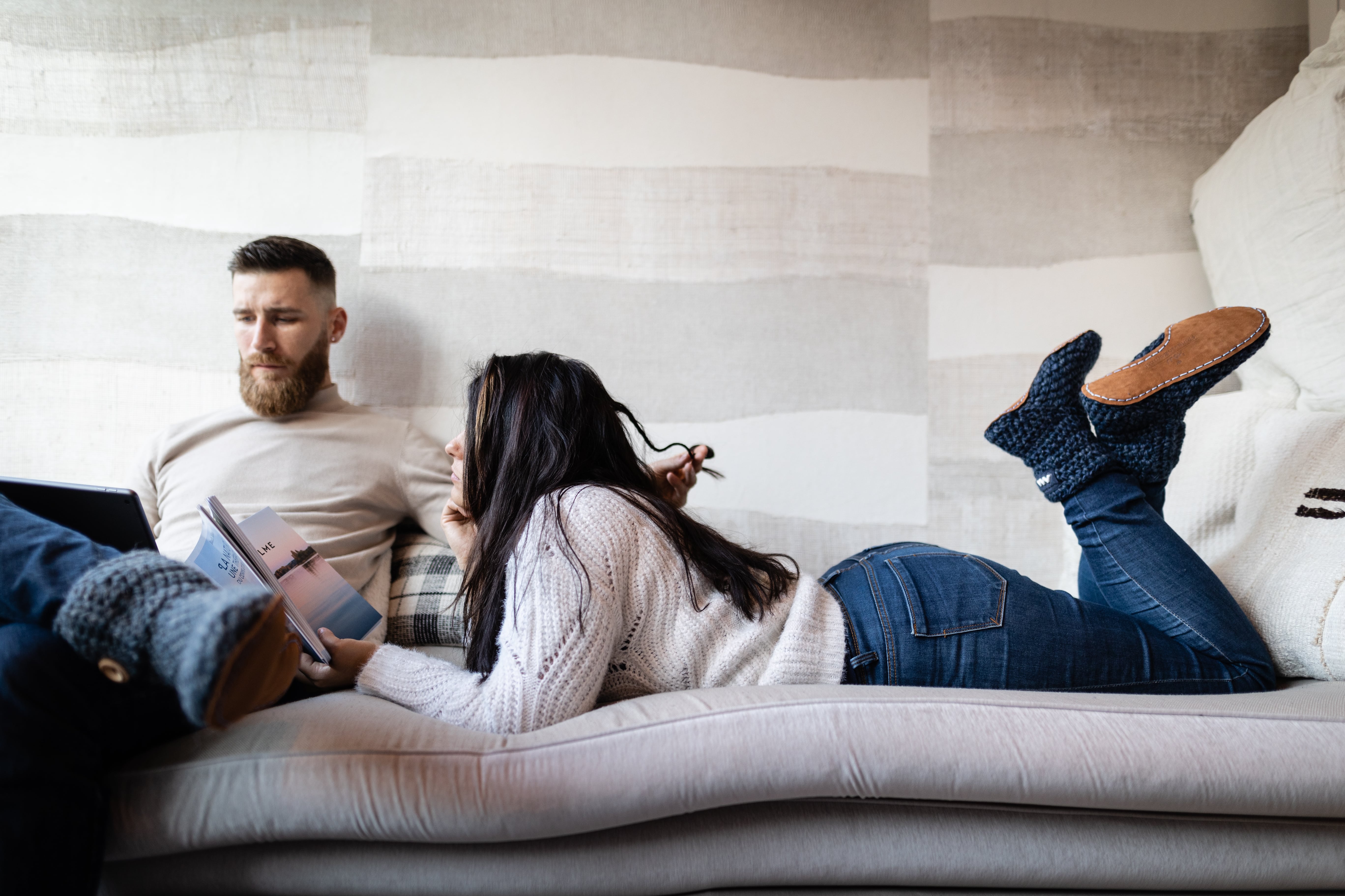 Couple sitting on a couch wearing slippers. The woman is reading a magazine. 