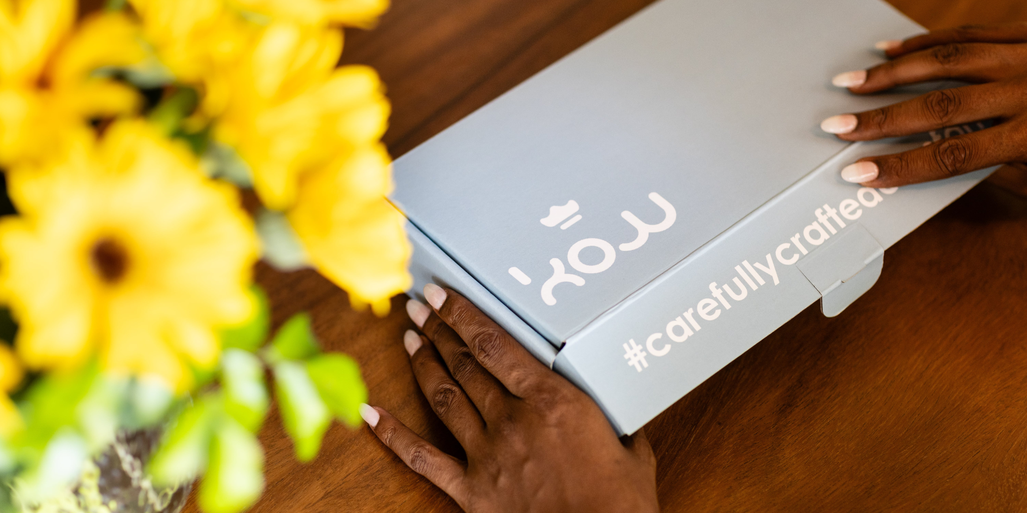 Blue box with 'KOW' branding on a wooden surface next to yellow gerberaflowers