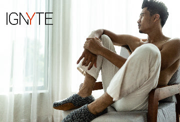 Man sitting on a chair with a towel draped over his shoulder, wearing slippers, with 'IGNYTE' branding.