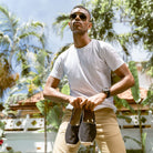 Man holding a pair of espadrilles with a tropical background