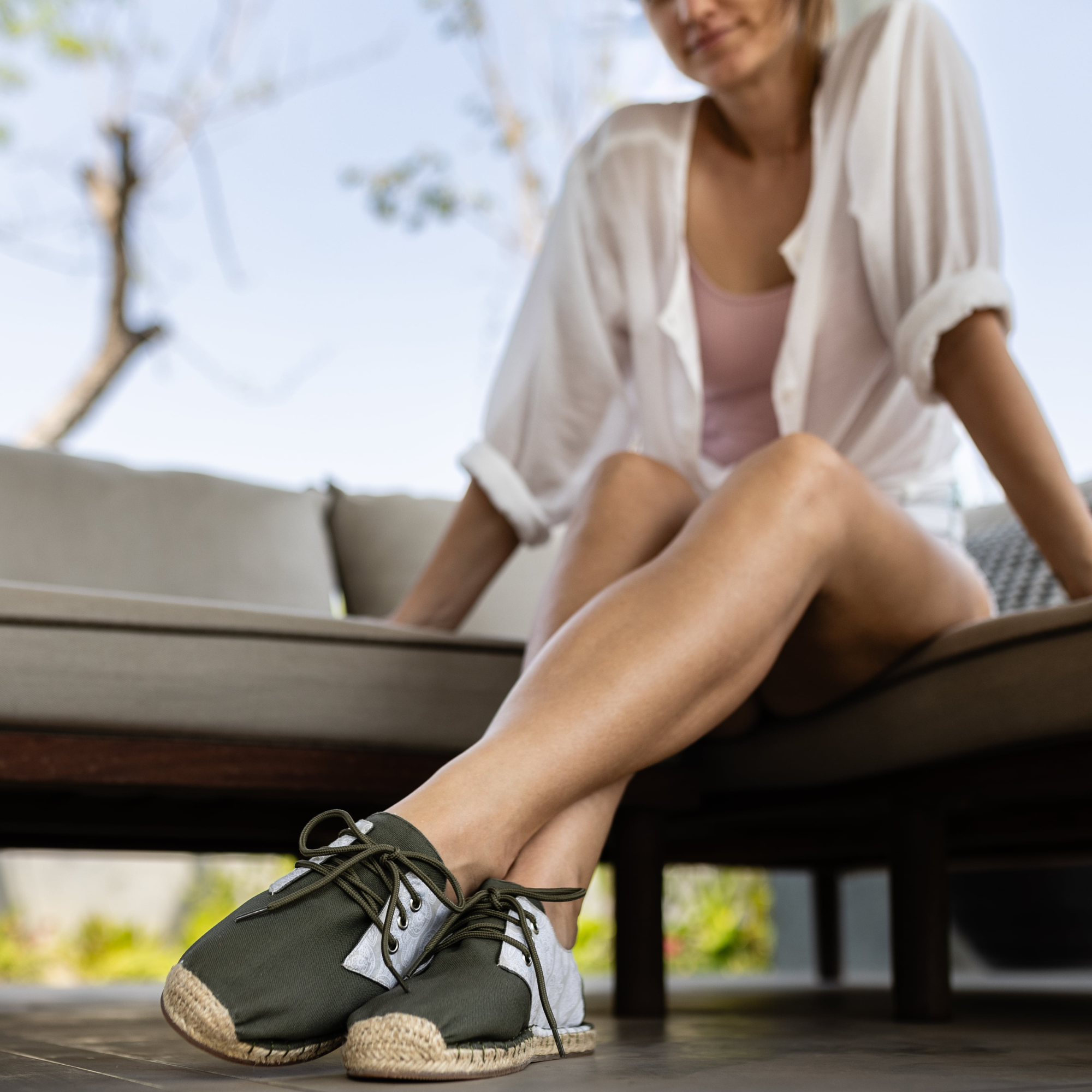 Woman sitting outdoors wearing khaki green espadrille sneakers.
