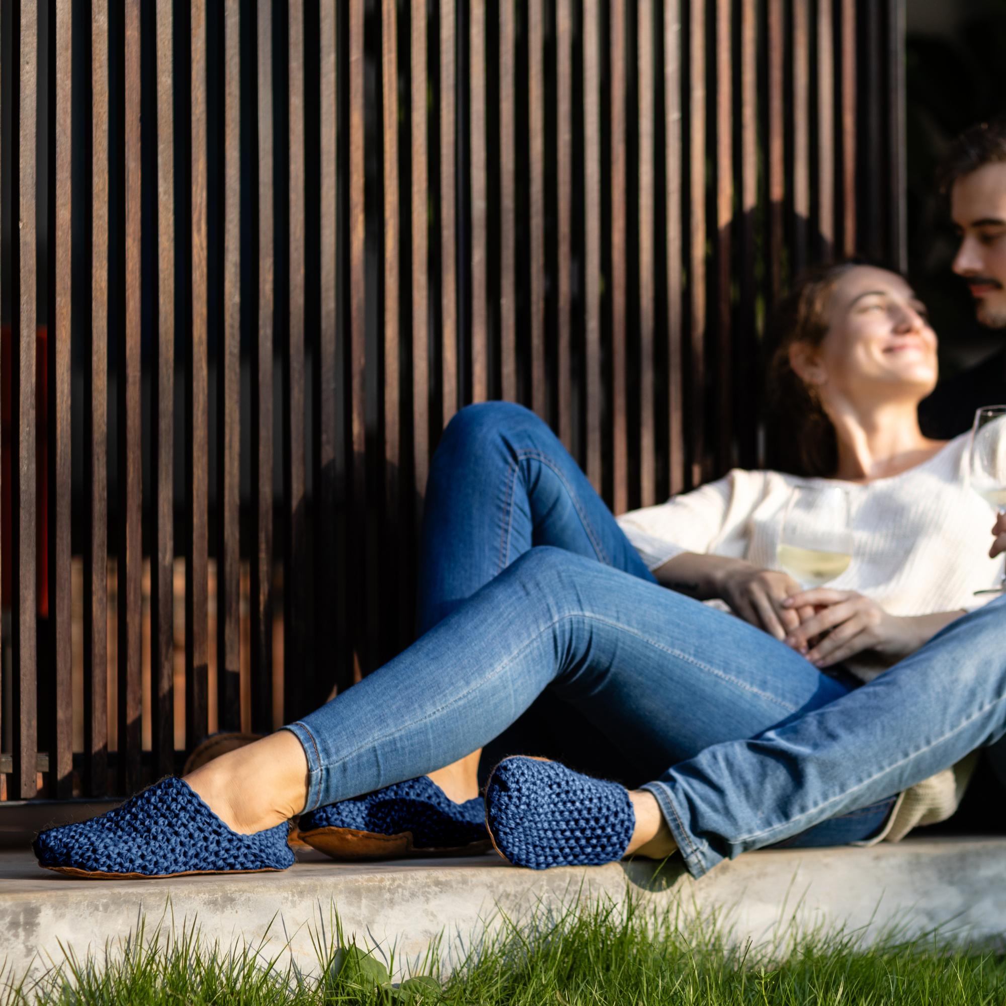 Two people sitting on a ledge wearing little blue slippers and jeans.