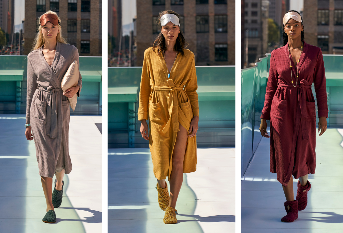 Three women in different colored dresses walking on a rooftop with cityscape background for New York Fashion Week