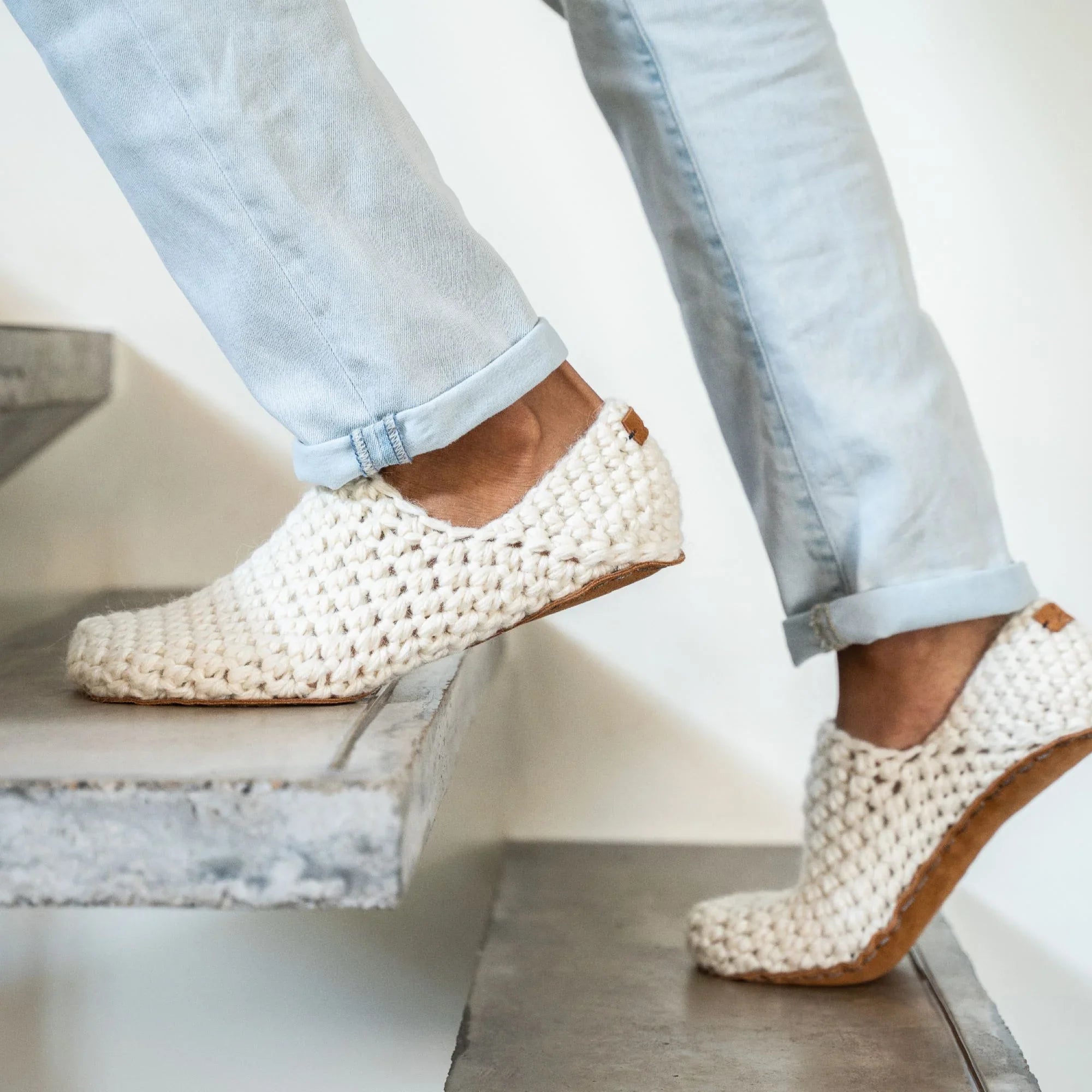 Person climbing stairs wearing white crocheted house shoes worn with light blue jeans