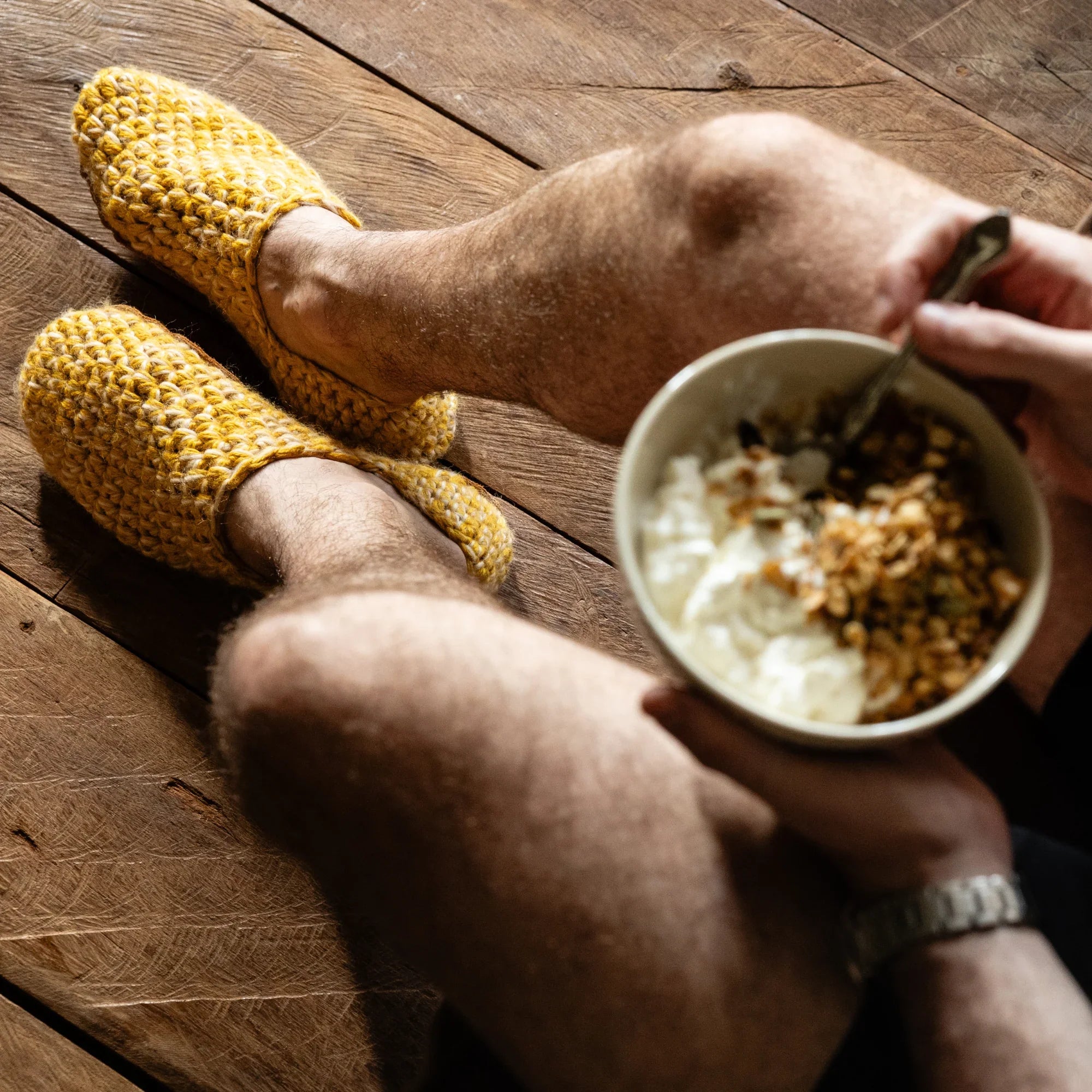 Person post workout sitting on a wooden floor wearing yellow wool slippers and holding a bowl of cereal.