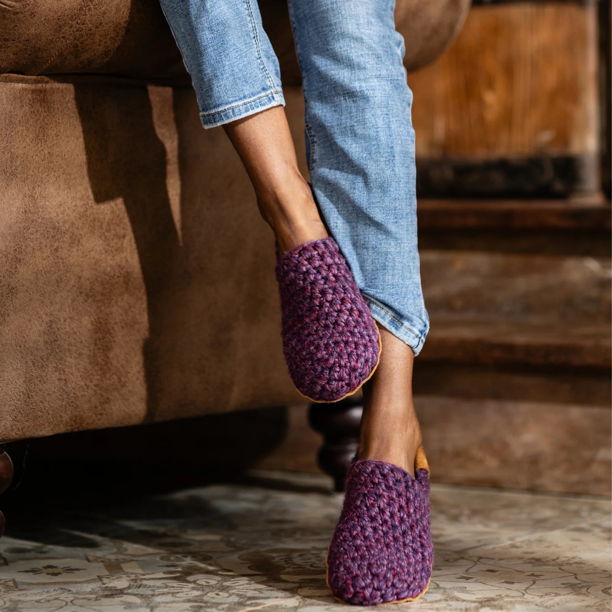 Person wearing handmade purple crocheted slippers on a tiled floor.