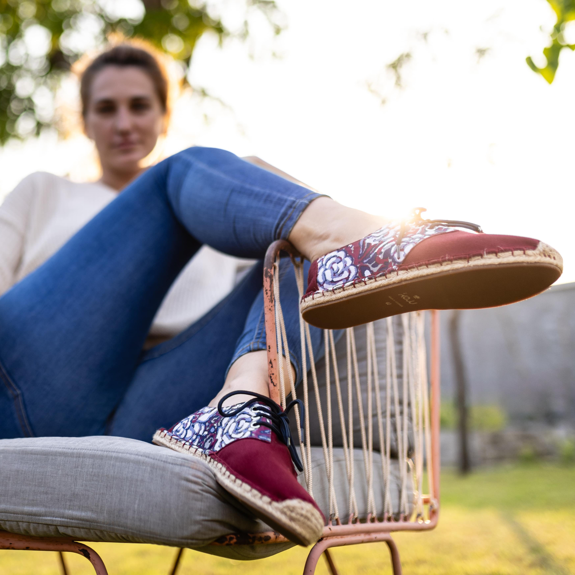 Woman wearing red lace-up espadrilles with floral patterns sitting outdoors.