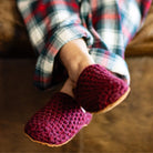 Person wearing maroon red crocheted slippers with a plaid pajamas