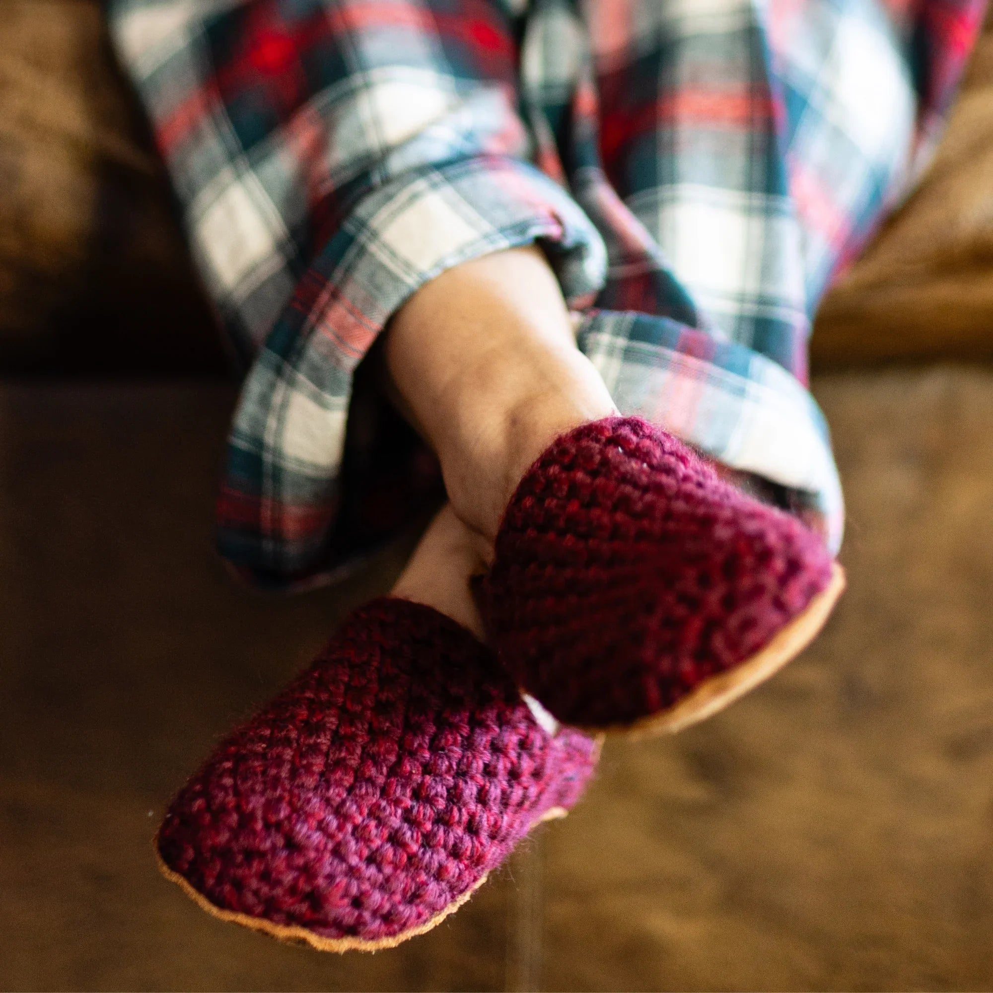 Person wearing maroon red crocheted slippers with a plaid pajamas