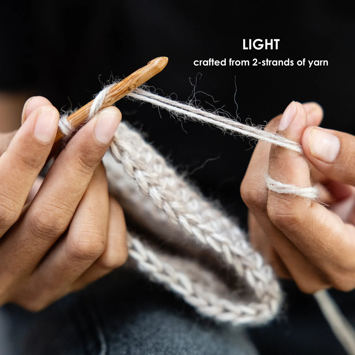 Close-up of hands knitting with a wooden crochet hook and light cream yarn, with text reading 'LIGHT crafted from 2-strands of yarn' on a dark background.