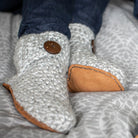Close-up of gray knitted slippers with leather soles on a patterned bedding.