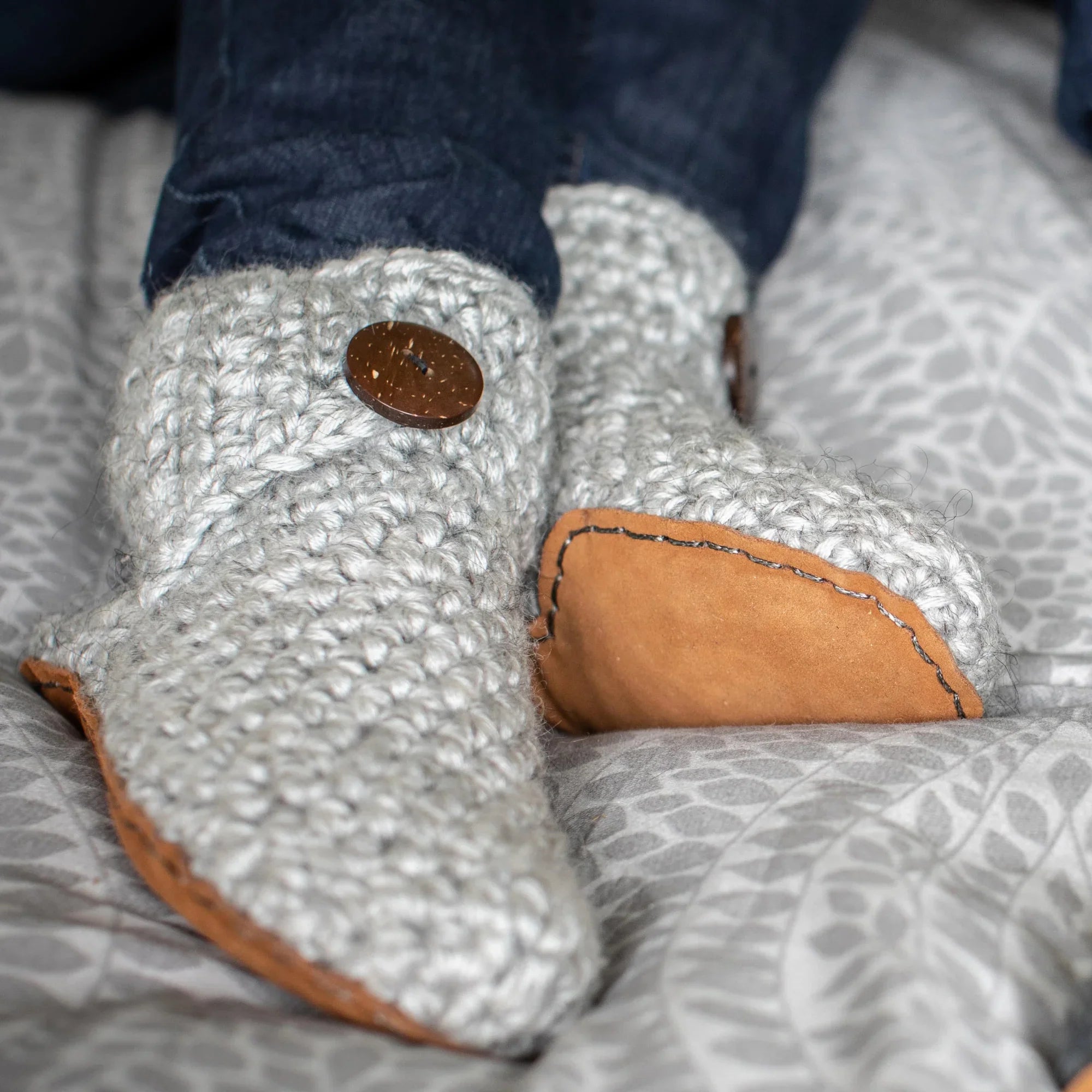 Close-up of gray knitted slippers with leather soles on a patterned bedding.