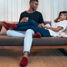 Two people sitting on a couch wearing red knitted slippers in a living room setting.