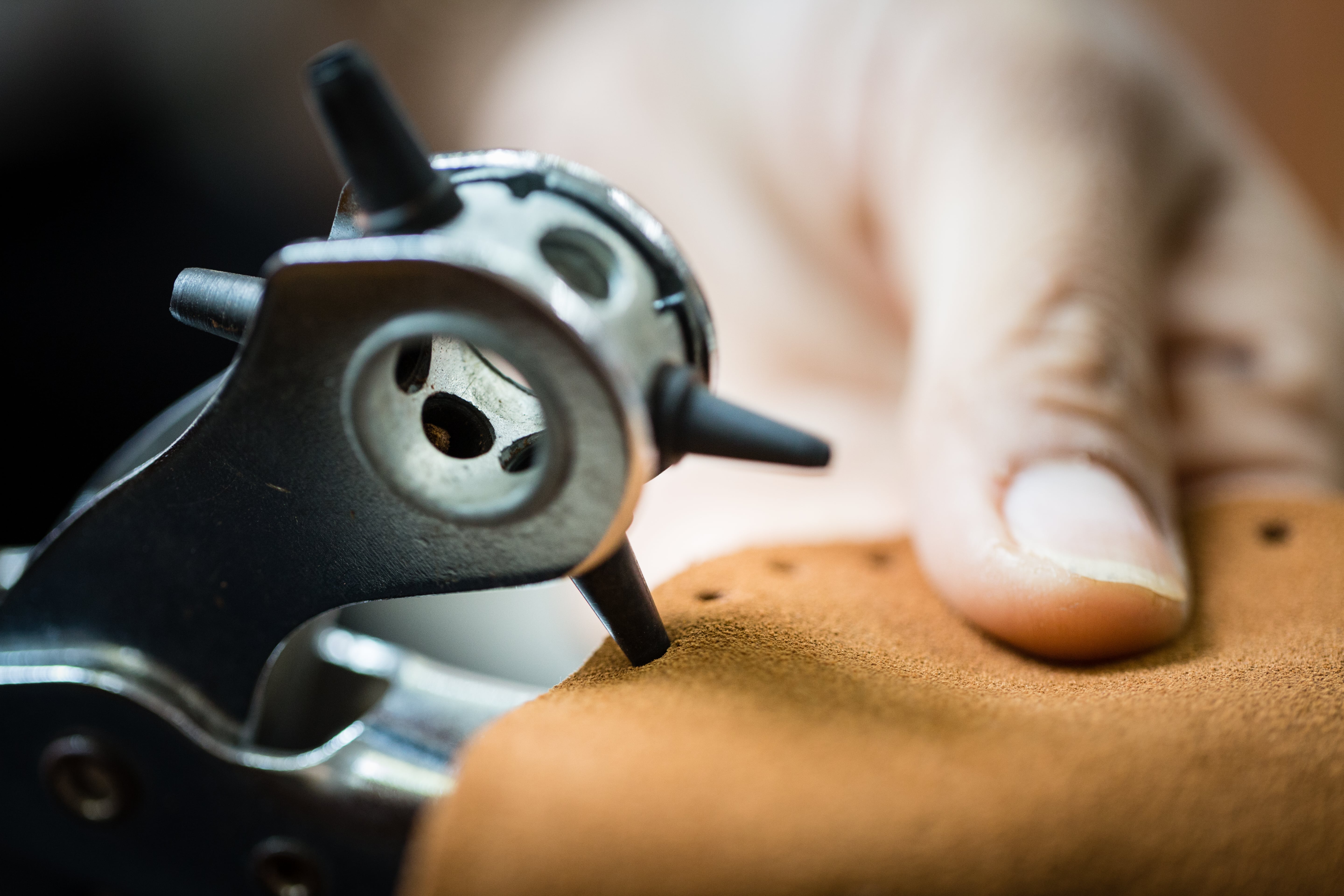 Close up of creating holes in leather slipper base to connect the wool slipper