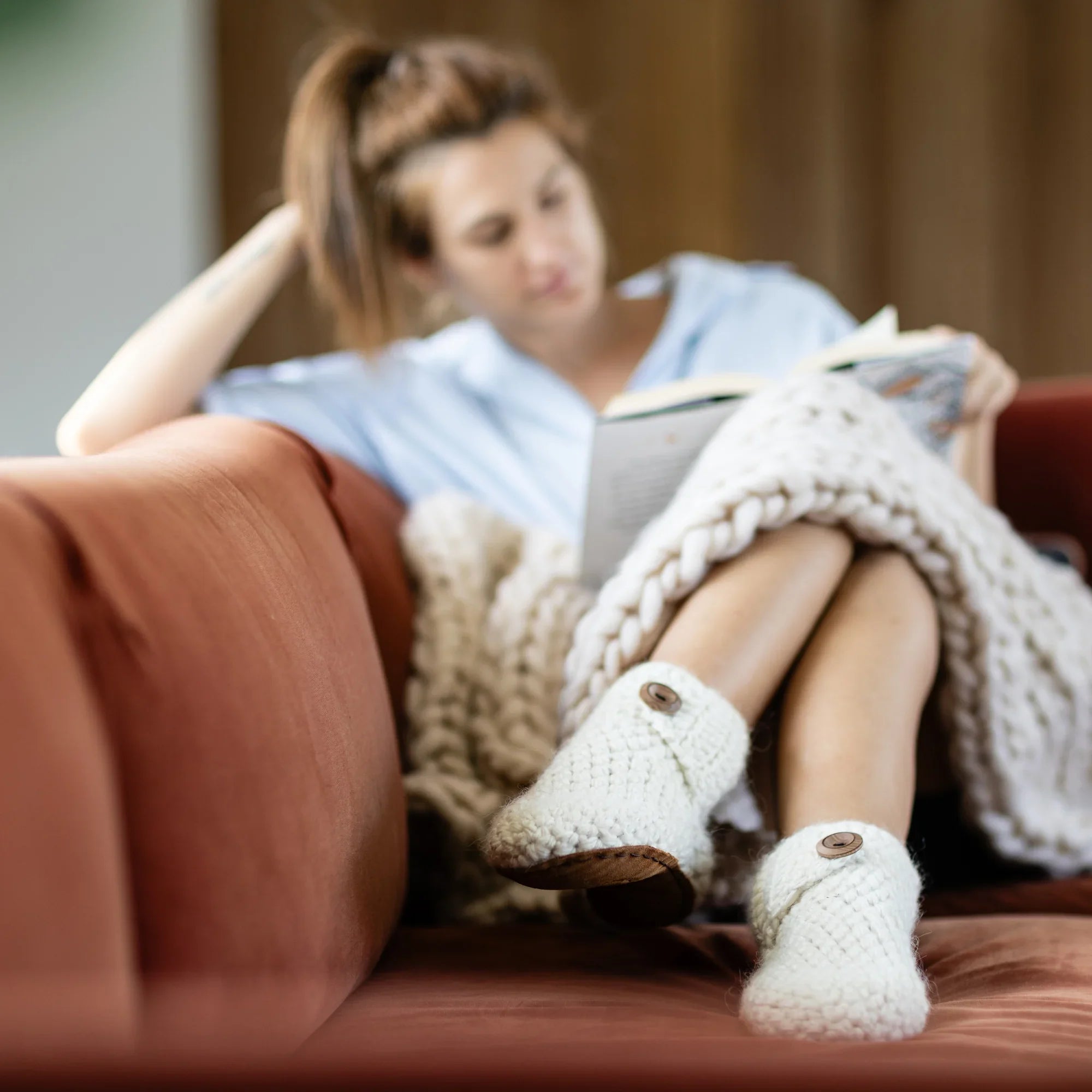 Woman on couch reading a book wearing classic white high top bootie wool slipper by Kingdom of Wow